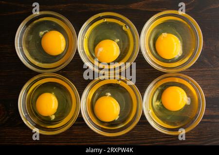 Uova incrinate nelle ciotole di preparazione: Sei uova incrinate in piccole ciotole di vetro su un tavolo di legno Foto Stock