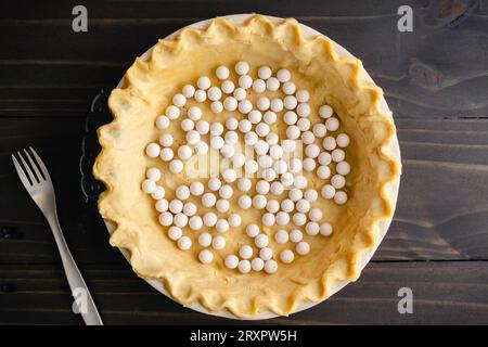 Impasto in crosta di torta non cotto con bordi schiacciati in una padella con pesi della torta: Impasto crudo con bordi crimpati in un piatto di ceramica profondo con pesi a torta in ceramica Foto Stock