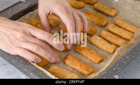 Teglia da forno con bastoncini di pesce in primo piano sul tavolo da cucina. Croccante delizioso leggermente impanato con pangrattato bastoncini di pesce primo piano Foto Stock