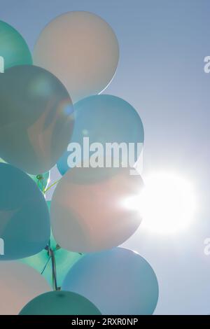 Palloncini blu, verdi, turchesi e bianchi che fluttuano all'aperto in cielo blu, retroilluminati dal sole a North Vancouver, Canada Foto Stock