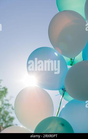 Palloncini blu, verdi, turchesi e bianchi che fluttuano all'aperto in cielo blu, retroilluminati dal sole a North Vancouver, Canada Foto Stock