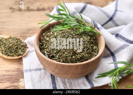 Dragoncello fresco e asciutto in ciotola su tavolo di legno, primo piano Foto Stock