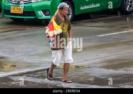 SAMUT PRAKAN, THAILANDIA, 20 settembre 2023, Un uomo porta un bastone con ghirlande di fiori appese in vendita Foto Stock