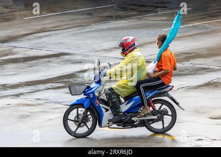 SAMUT PRAKAN, THAILANDIA, 20 settembre 2023, Moto taxi sta guidando una donna con un carico su una strada bagnata Foto Stock