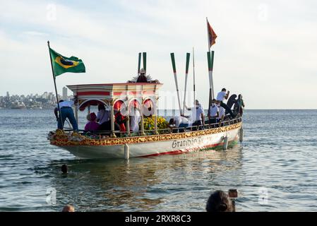 Salvador, Bahia, Brasile - 31 dicembre 2021: Si vede la barca Galiota lasciare la spiaggia con la statua di Gesù Cristo, il signore dei marinai, nel c Foto Stock