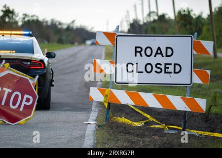 Auto di pattuglia della polizia al cartello segnaletico dei lavori stradali e barriera di sicurezza sulla strada cittadina durante i lavori di manutenzione e riparazione Foto Stock