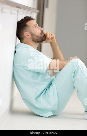 depresso assistente medico maschio seduto sul pavimento Foto Stock