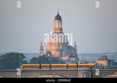 Dresda, Germania. 27 settembre 2023. Un tram della Dresdner Verkehrsbetriebe (DVB) guida al mattino di fronte al paesaggio della città vecchia con la Frauenkirche (l) e la cupola della Kunstakedmie con l'angelo 'fama' sopra il Albertbrücke. Credito: Robert Michael/dpa/Alamy Live News Foto Stock