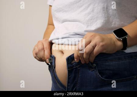 Primo piano di una giovane donna in sovrappeso che cerca di vestirsi in jeans Foto Stock