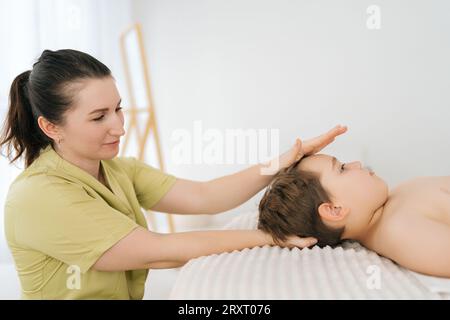 Ritratto laterale di un bambino di cinque anni sottoposto a trattamento osteopatico o chiropratico in clinica pediatrica. Fisioterapista femminile professionista Foto Stock