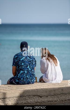 giovani coppie sedute su un muro insieme guardano al mare sognando ad occhi aperti mentre si trovano in vacanza nel mediterraneo sull'isola greca di zante o zante. Foto Stock