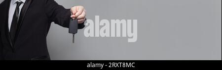 Giovane uomo d'affari adulto in completo che regala le chiavi di un'auto su sfondo grigio, primo piano Foto Stock
