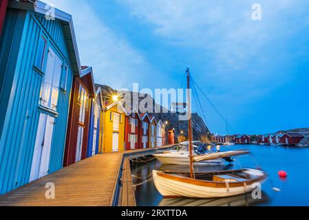 Capanne da pesca colorate con barca di legno ormeggiata al molo al tramonto, Smogen, Bohuslan, Vastra Gotaland, Svezia occidentale, Svezia, Scandinavia, Europa Foto Stock