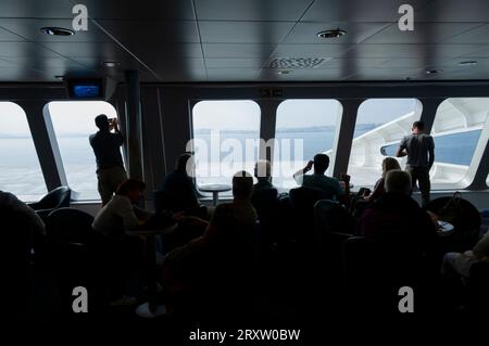 Silhouette di un gruppo di passeggeri su un traghetto mentre guardano attraverso i finestrini del ponte della nave vicino alla costa del Marocco Foto Stock