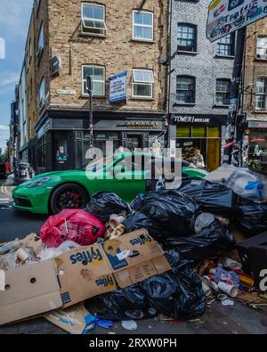 Un'auto veloce passa attraverso i rifiuti accumulati sul Brick Lane di Londra a Tower Hamlets. Foto Stock