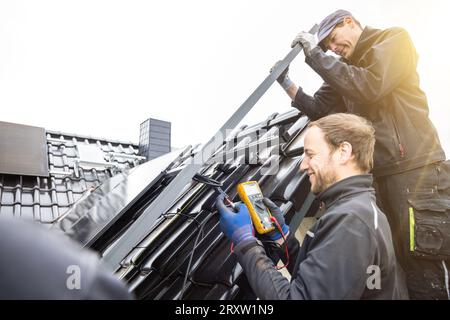 Team di tecnici che installano e testano pannelli solari sul tetto di una casa Foto Stock