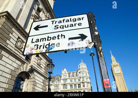 Indicazioni stradali per Londra con le frecce per Trafalgar Square e Lambeth Bridge. Adesivi d'arte visibili utilizzati dagli artisti di strada per promuovere il loro lavoro. Foto Stock