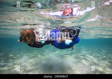 Due amanti dello snorkeling in acque cristalline che guardano la macchina fotografica che galleggia sulla superficie dell'acqua Foto Stock