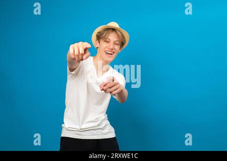 Ehi. Headshot di allegro sereno spensierato giovane uomo in casual bianco t-shirt punti dita di entrambe le mani a voi, studio ritratto isolato su Foto Stock