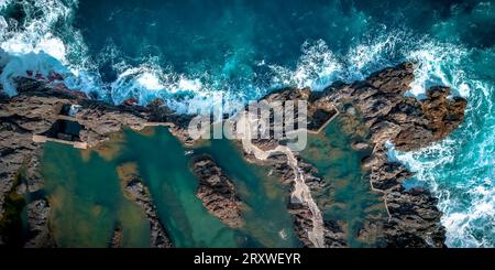 Vista panoramica a volo d'uccello delle persone che nuotano nelle piscine naturali di lava di Porto Moniz, Madeira, Portogallo, mentre il mare infuria intorno a loro Foto Stock