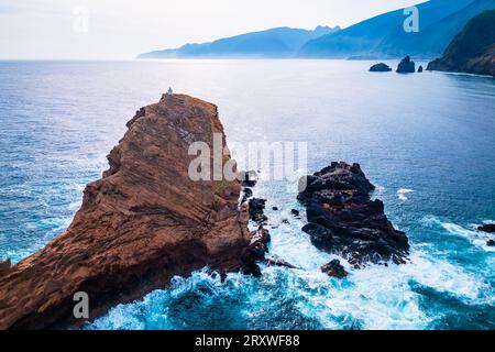 Vista aerea panoramica della piccola isola di Ilheú Mole al largo di Porto Moniz, Madeira, Portogallo, con un piccolo faro automatico autosufficiente sulla sua cima Foto Stock
