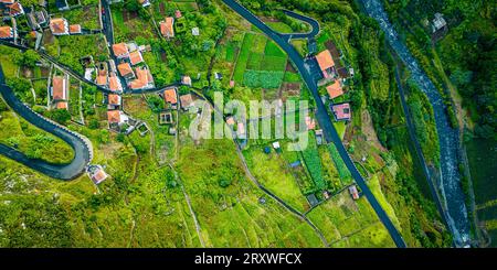 Splendida vista panoramica a volo d'uccello del piccolo villaggio di montagna di Ribeira da Janela a Madeira, Portogallo, che si estende lungo una montagna Foto Stock