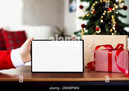 Natale, Capodanno, sfondo con spazio per la copia per il design. Mano Babbo Natale che tiene lo schermo vuoto della tavoletta bianca. Mockup per il montaggio del posizionamento dei prodotti. O Foto Stock