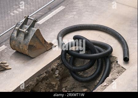 tubo corrugato nero per cavi elettrici e benna per escavatore Foto Stock