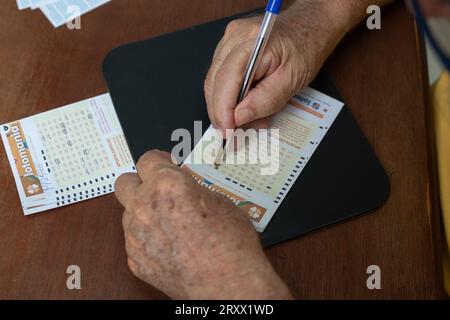 Goiânia, Goias, Brasile – 26 settembre 2023: Primo piano sulle mani di un anziano che sta segnando i numeri su una carta della lotteria. Foto Stock