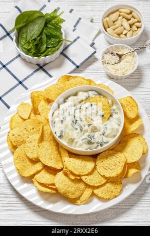 salsa cremosa di carciofi spinaci alle mandorle con patatine fritte su piatto bianco su tavola di legno bianco con ingredienti, vista verticale dall'alto Foto Stock