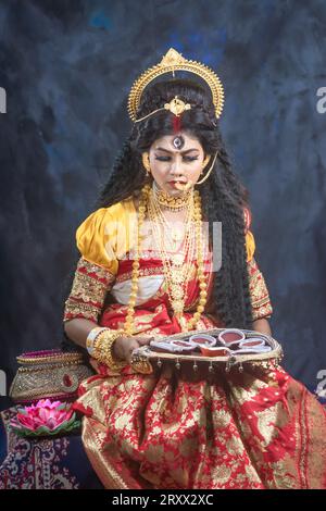 Ritratto della bellissima ragazza indiana di Durga Idol Agomoni Concept foto al coperto che indossa il tradizionale sari indiano, gioielli in oro e braccialetti. Maa Durga Foto Stock