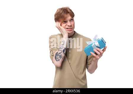 un giovane ragazzo dai capelli rossi con gli occhiali e una camicia marrone decide chi regalare una confezione regalo con una sorpresa. Foto Stock