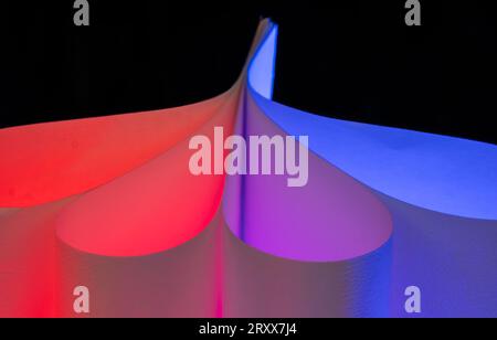 Primo piano delle forme curve di colore rosso e blu realizzate per normali fogli di carta bianca e luci colorate Foto Stock