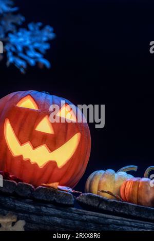 Un sorridente Jack o Lanterna seduto su un vecchio portico di legno con piccole zucche e foglie cadute come Halloween. Foto Stock