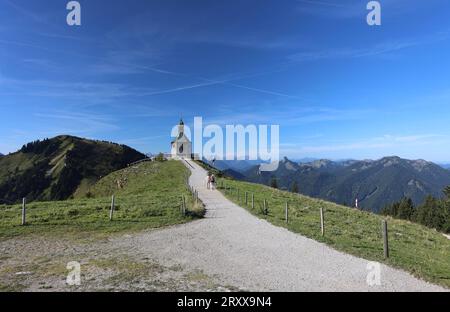 Wallberg, Bayern, Deutschland 27. Settembre 2023: Hier der Blick von der Bergstation der Wallbergbahn auf das bekannte Kirchlein, Kapelle Heilig Kreuz, Fotomotiv, Tourismus, wandern, spazieren, Ausblick, Panorama, Rottach-Egern, Touristen, Links der Setzberg, rechts Zugspitze und Ross und Buchstein *** Wallberg, Baviera, Germania 27 settembre 2023 qui la vista dalla stazione a monte della Wallbergbahn alla famosa chiesetta, cappella di Santa Croce, motivi fotografici, turismo, escursioni, passeggiate, vista, panorama, Rottach Egern, turisti, sinistra Setzberg, destra Zugspitze e Ross e Buchstein Foto Stock