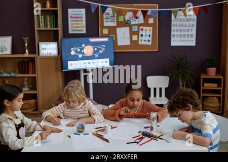 Gruppo eterogeneo di bambini piccoli che fanno arte e artigianato seduti al tavolo in classe prescolare, spazio fotocopie Foto Stock