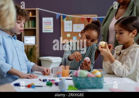 Diversi gruppi di bambini piccoli che dipingono uova di Pasqua durante le lezioni di arte e artigianato in età prescolare Foto Stock