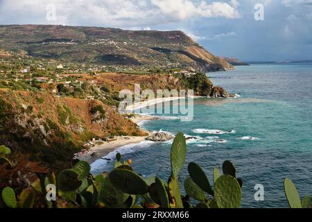 Golfo turchese di Capo Vaticano, Calabria, Italia meridionale. Spiaggia sabbiosa, montagne e piante verdi, cielo blu, nuvole bianche, piattaforma di scogliere Foto Stock