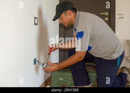 Immagine di un elettricista addetto alla riparazione e all'installazione di una presa elettrica domestica. Presa di alimentazione fai da te. Foto Stock
