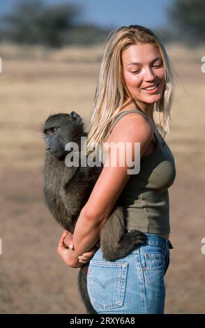 Giovane donna con giovane Anubis Baboon (Papio anubis), Namibia (Papio cynocephalus anubis), Junge Frau mit Anubis-Pavian, Jungtier, Namibia / Foto Stock