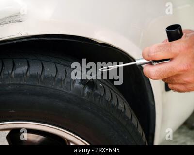 Concetto: Meccanica automobilistica. Dettaglio della mano, dell'attrezzo e dello pneumatico con tappo appena installato e perforato per perdite d'aria. Foto Stock