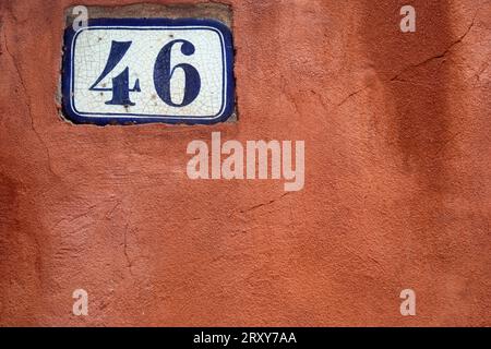 Il numero 46 in blu scuro su un pannello bianco contro una parete verniciata di rosso, girato da vicino riempiendo la cornice ma lasciando spazio per la copia. Foto Stock