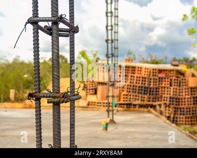 Vista delle barre strutturali in ferro per le colonne in calcestruzzo di una costruzione rurale, con una pila di mattoni di argilla cavi sul retro. Foto Stock