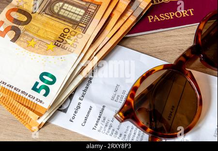 Un concetto di viaggio, vacanza e scambio di denaro con banconote in euro, passaporto e occhiali da sole sopra una ricevuta di cambio valuta. Foto Stock