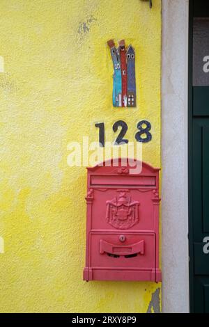 Burano, Veneto, Italia, settembre 2023, primo piano di una cassetta postale rossa contro un muro giallo pallido Foto Stock