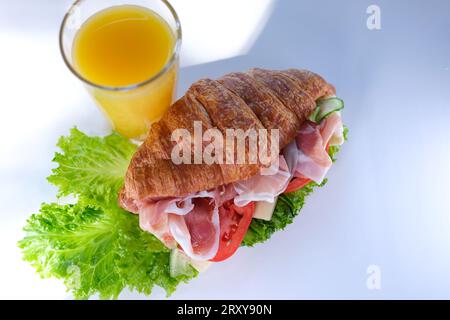 Panino croissant con prosciutto di carne con foglie di lattuga al pomodoro verdure cibo sano e costoso ricchi pezzi di formaggio a colazione in Francia su un piatto bianco. ristorante costoso Foto Stock