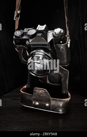 Una vecchia fotocamera reflex con telemetro a film in una custodia squallida su sfondo scuro Foto Stock