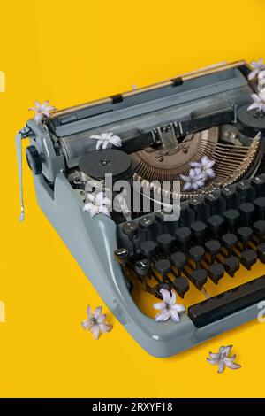 Macchina da scrivere vintage con fiori di lilla su sfondo giallo Foto Stock