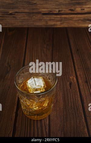 Un cristallo trasparente riempito di liquore color miele con alcuni cubetti di ghiaccio Foto Stock
