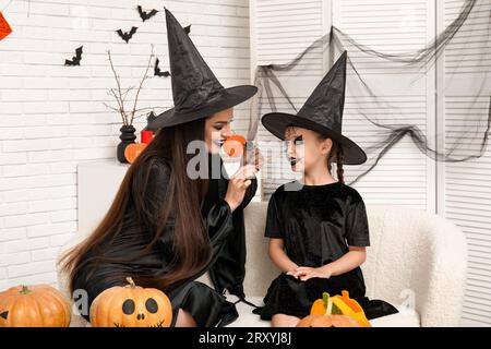 Madre vestita per Halloween dipingendo il volto della sua bambina a casa Foto Stock